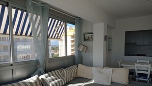 Una habitación acogedora con un sofá a rayas, una mesita pequeña y vistas a edificios a través de amplias ventanas.