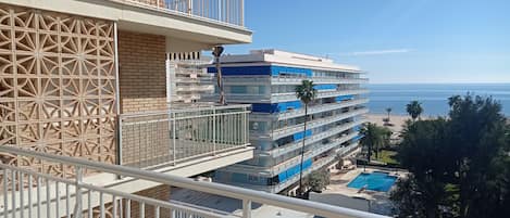 A multi-story hotel with balconies, a pool, and a beach view.
