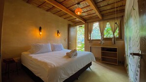 A bedroom with a wooden ceiling, a bed with white linens, two wall-mounted lights, and a window with curtains.
