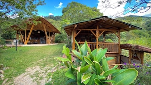 A rustic wooden structure with a covered patio area, surrounded by lush greenery and a clear blue sky.