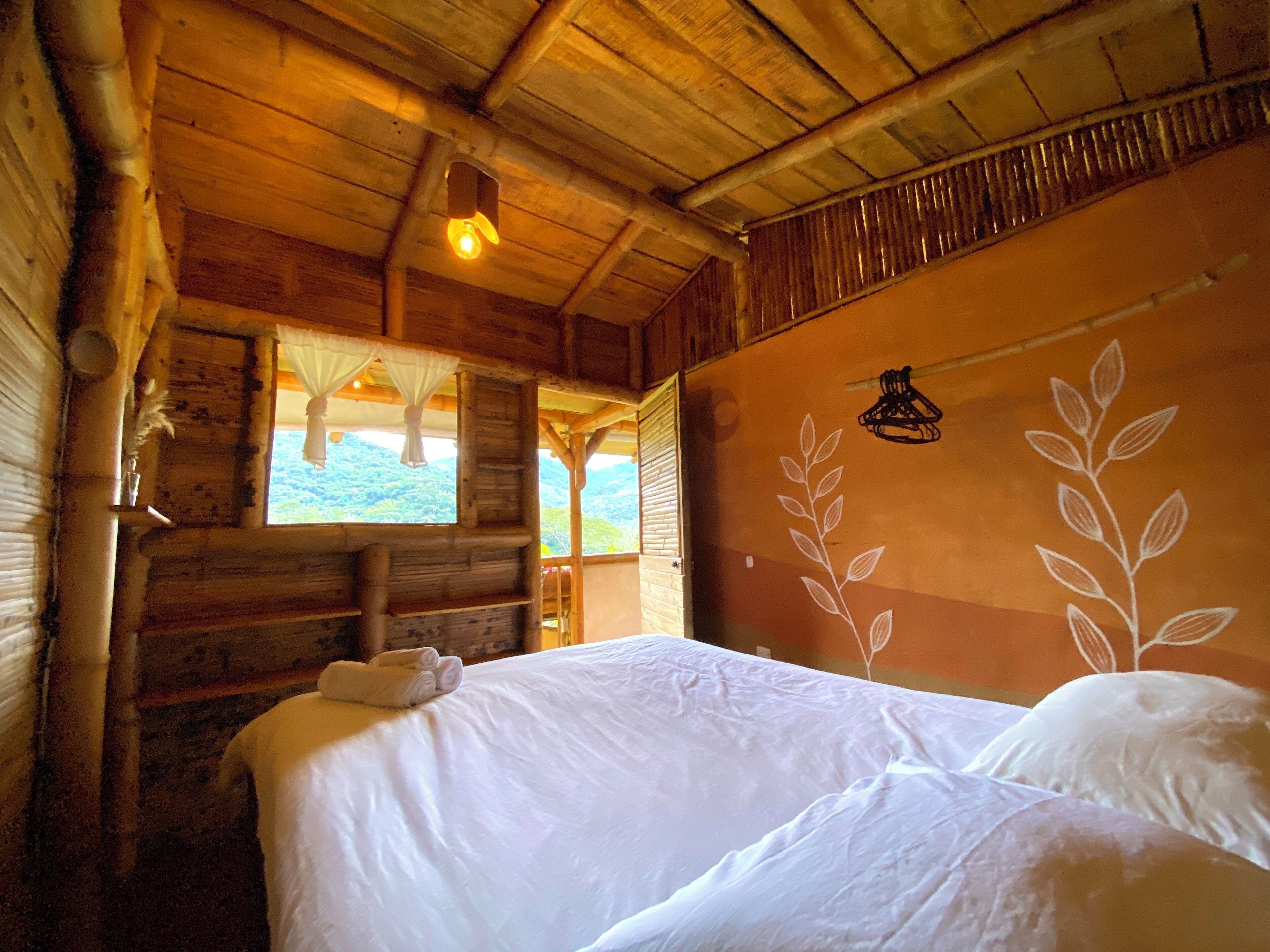 Un dormitorio de cabaña de madera con una cama, una ventana con cortinas y una pared con un diseño de hojas.
