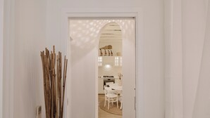 A hallway leading to a dining area with a white table and chairs, a kitchen in the background, and a decorative wooden structure on the left.