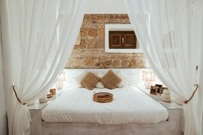 A bedroom with a stone wall, a bed with white bedding, two brown pillows, a wicker basket, and a wooden cabinet. - Borgo Pio Vatican Luxury (Rome)