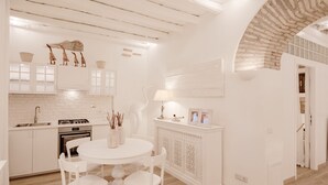 A modern kitchen with white cabinetry, a round dining table, and a brick archway.
