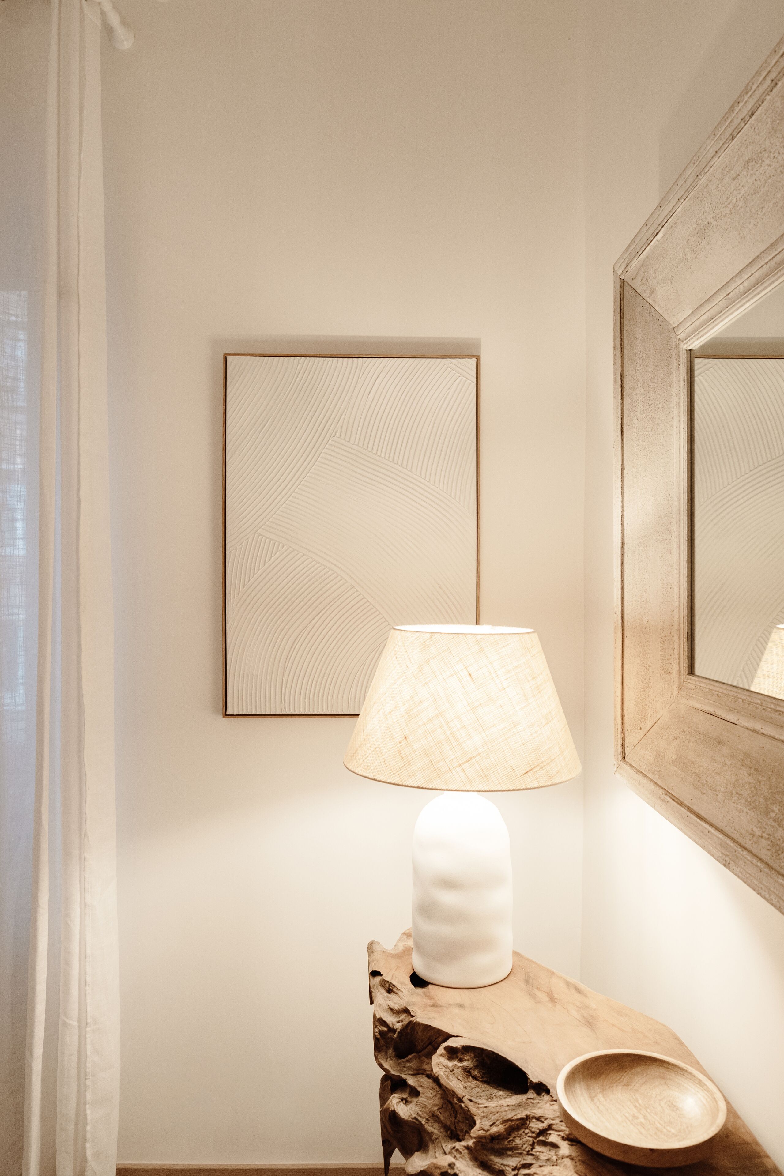 Un baño con una mesita de madera, una lámpara blanca, un cuadro enmarcado y un espejo.