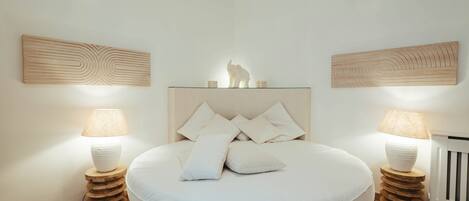 A bedroom with a round bed, two bedside tables with lamps, and wooden wall art above the bed.