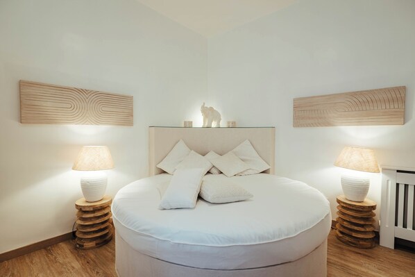 A bedroom with a round bed, two bedside tables with lamps, and wooden wall art above the bed. - Borgo Pio Vatican Luxury (Rome)