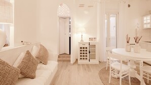 A spacious room with a white sofa, a dining table with chairs, and a kitchen area visible through an archway.