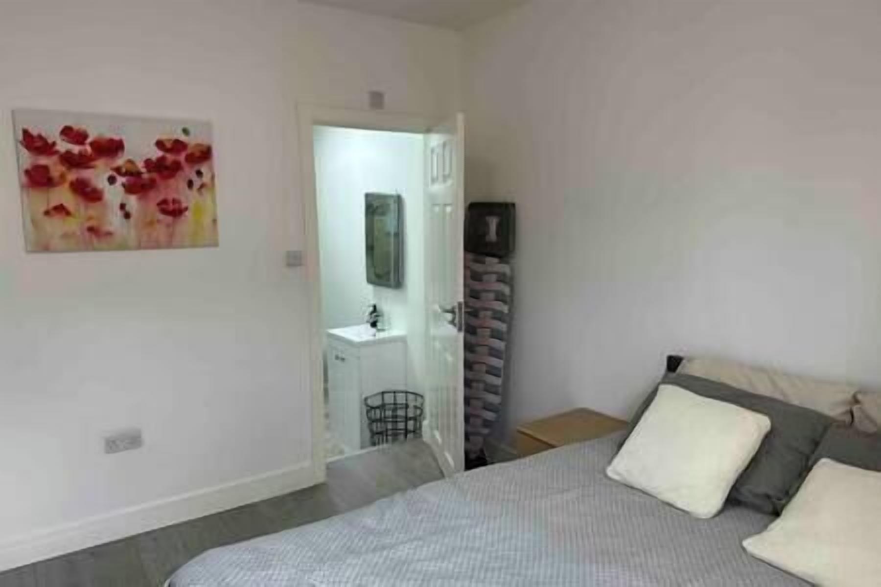 A bedroom with a bed, pillows, a nightstand, a mirror, and a door leading to a bathroom.