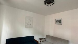 Ein Wohnzimmer mit einem dunkelblauen Sofa und einem hellgrauen Sofa, Holzboden und einer Deckenleuchte.
