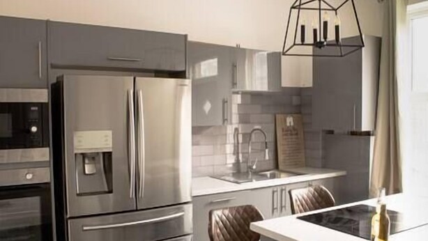Eine moderne Küche mit Edelstahlgeräten, einem Backofen, einem Kühlschrank, einer Spüle und einem Essbereich mit Stuhl und Tisch.