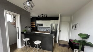 A modern kitchen with a black island, white cabinets, and stainless steel appliances. There are two bar stools and a potted plant. - Saint Sebastian Flat 704Duplex no Centro (Jaragua do Sul)