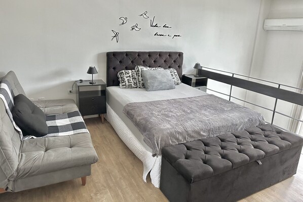 Un dormitorio moderno con una cama, un sofá, una mesita de noche y una pared decorada.