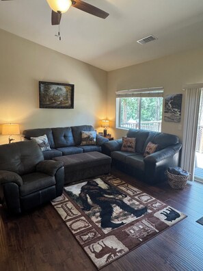 A living room with a sectional sofa, a rug with animal prints, a ceiling fan, and a window with a view of trees.