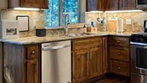 A kitchen with wooden cabinets, a dishwasher, a stove, and a window with a view of trees. - Pollock Pines - Family get away, 2 miles from Sly Park lake - Near Apple Hill

 (Pollock Pines)