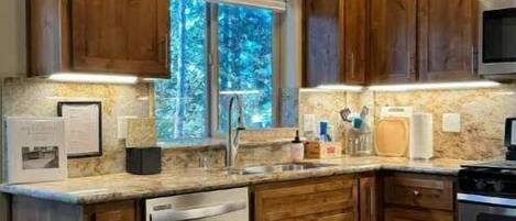 Una cocina con armarios de madera, lavavajillas, estufa y ventana con vistas a árboles.