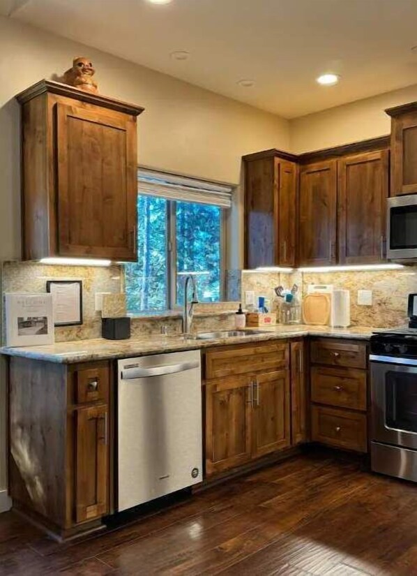 A kitchen with wooden cabinets, a dishwasher, a stove, and a window with a view of trees.