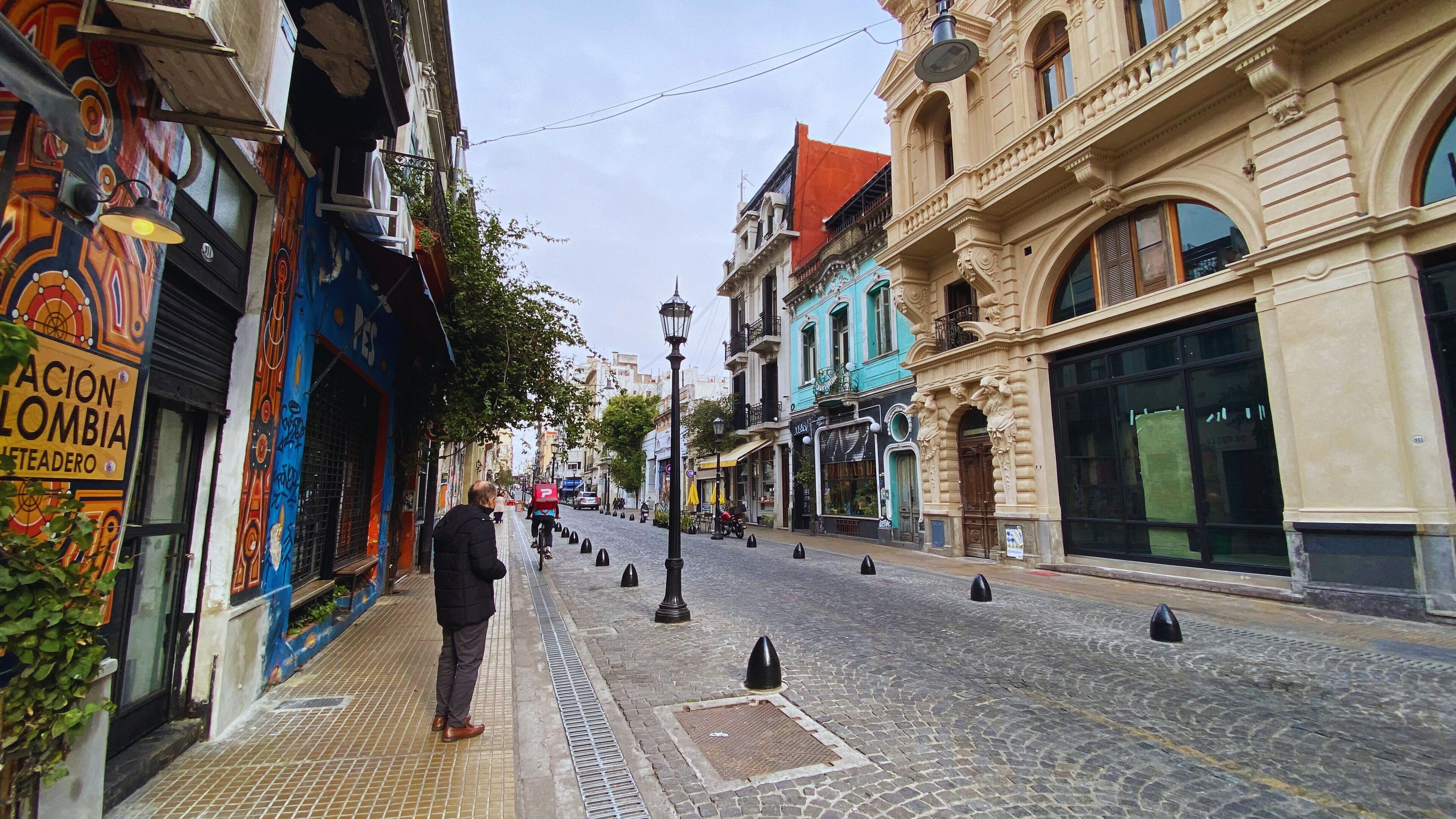 Una calle empedrada flanqueada por edificios, incluyendo un local comercial llamativo y un edificio con arquitectura ornamentada.
