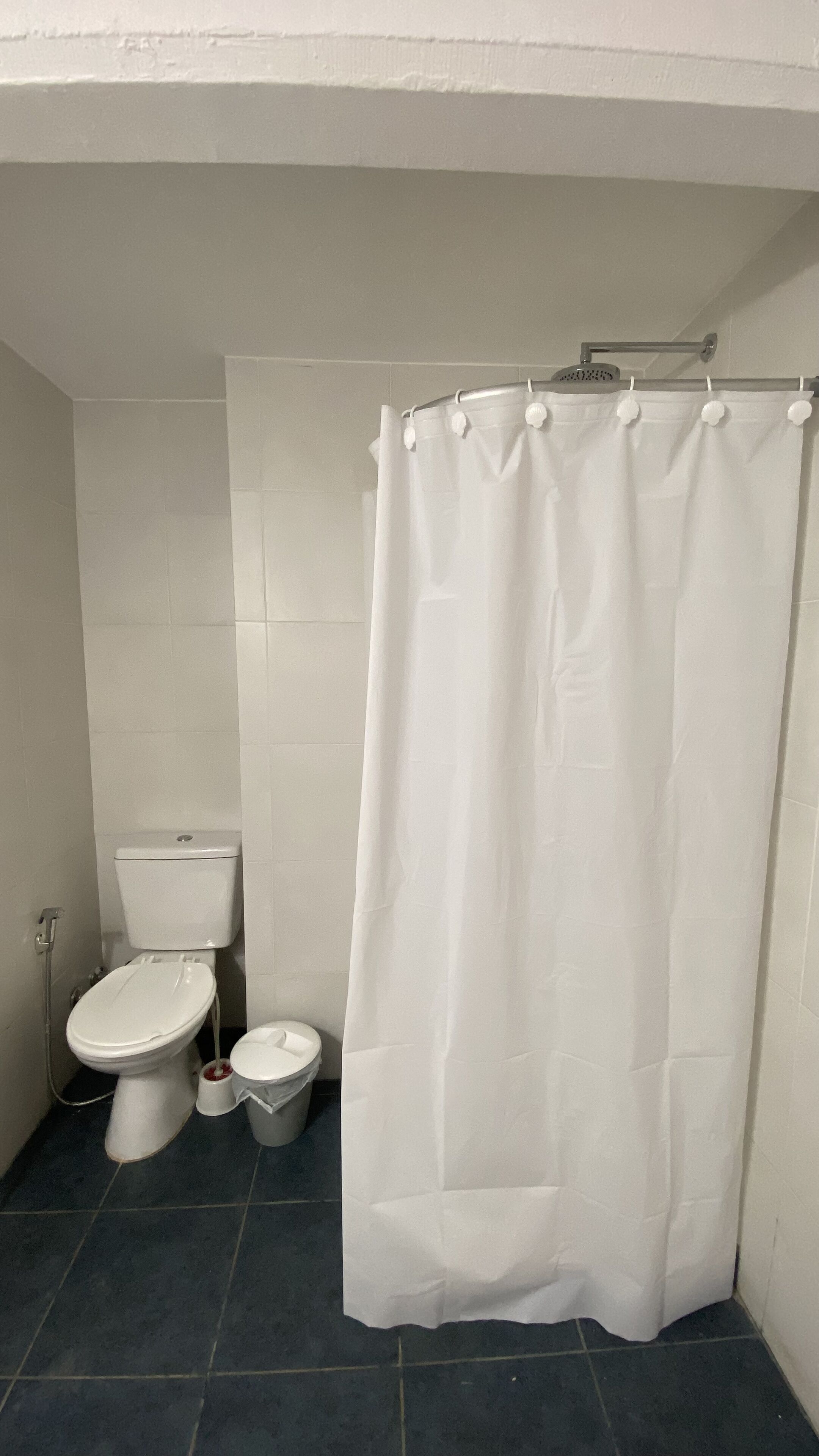Un baño pequeño y limpio con inodoro, lavamanos y cortina de ducha, todo en blanco.