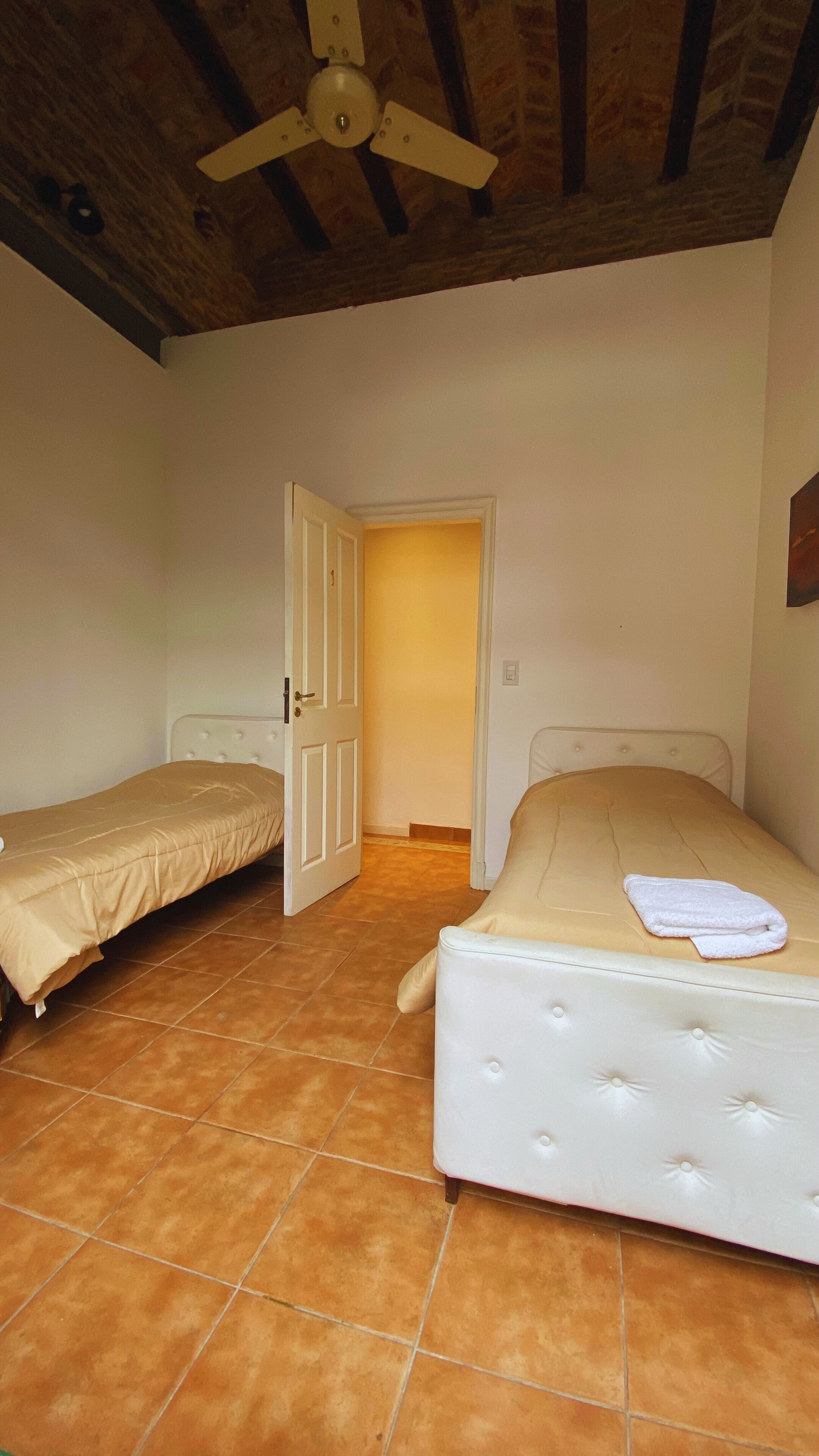 A room with two beds, a ceiling fan, and a door leading to another room.