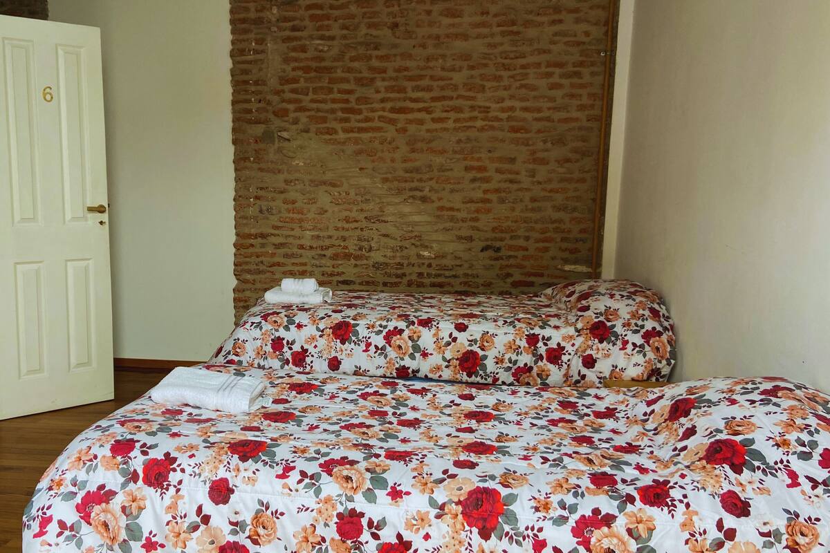 A room with a brick wall, a white door, and a bed with floral bedding.