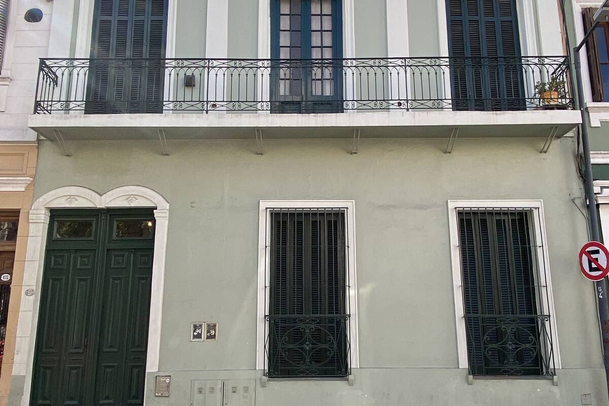 A two-story building with a balcony, a green door, and barred windows.