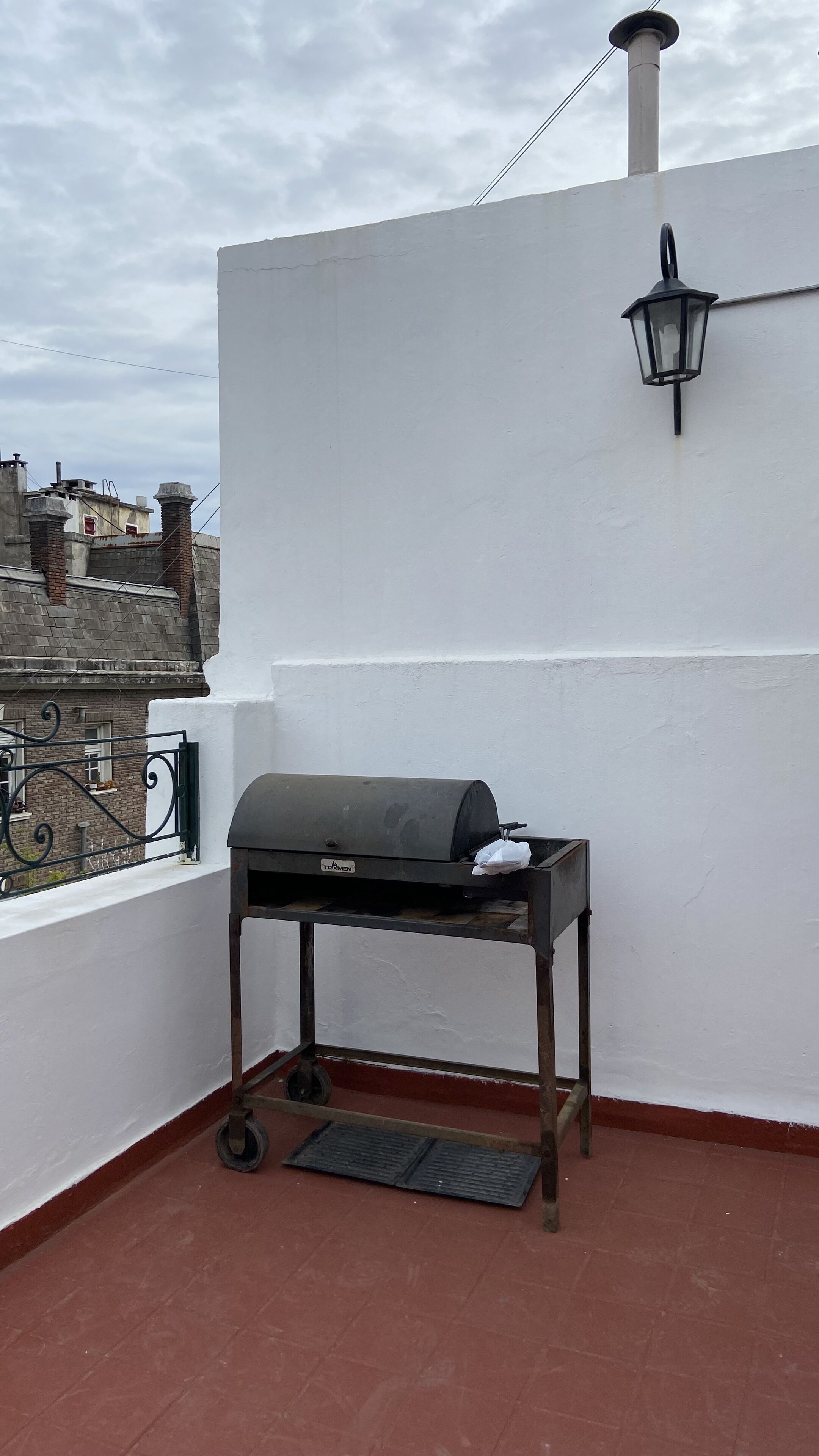 A rooftop with a grill, a lantern, and a view of buildings in the background.