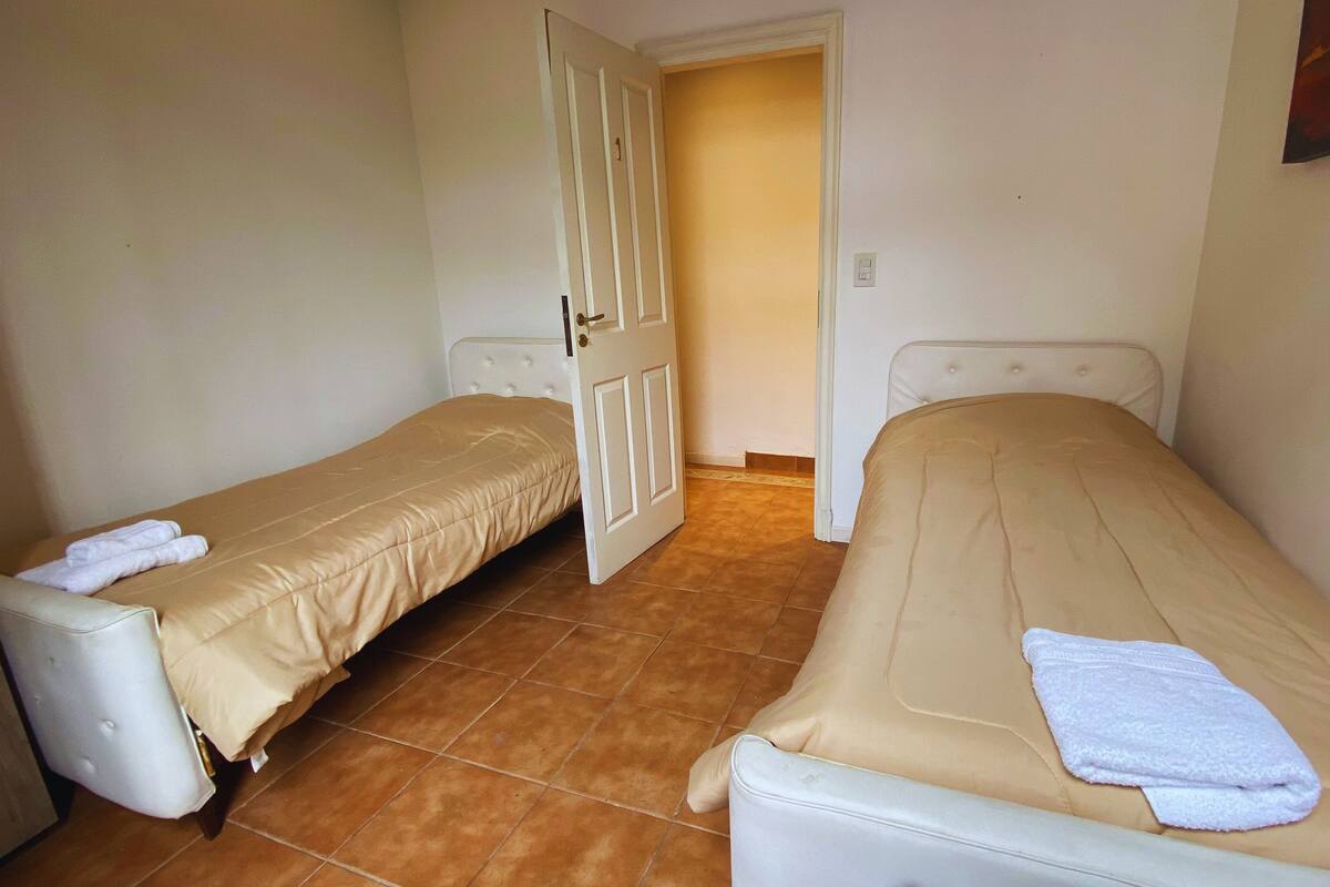 A small, clean room with two single beds, a white door, and a tiled floor.