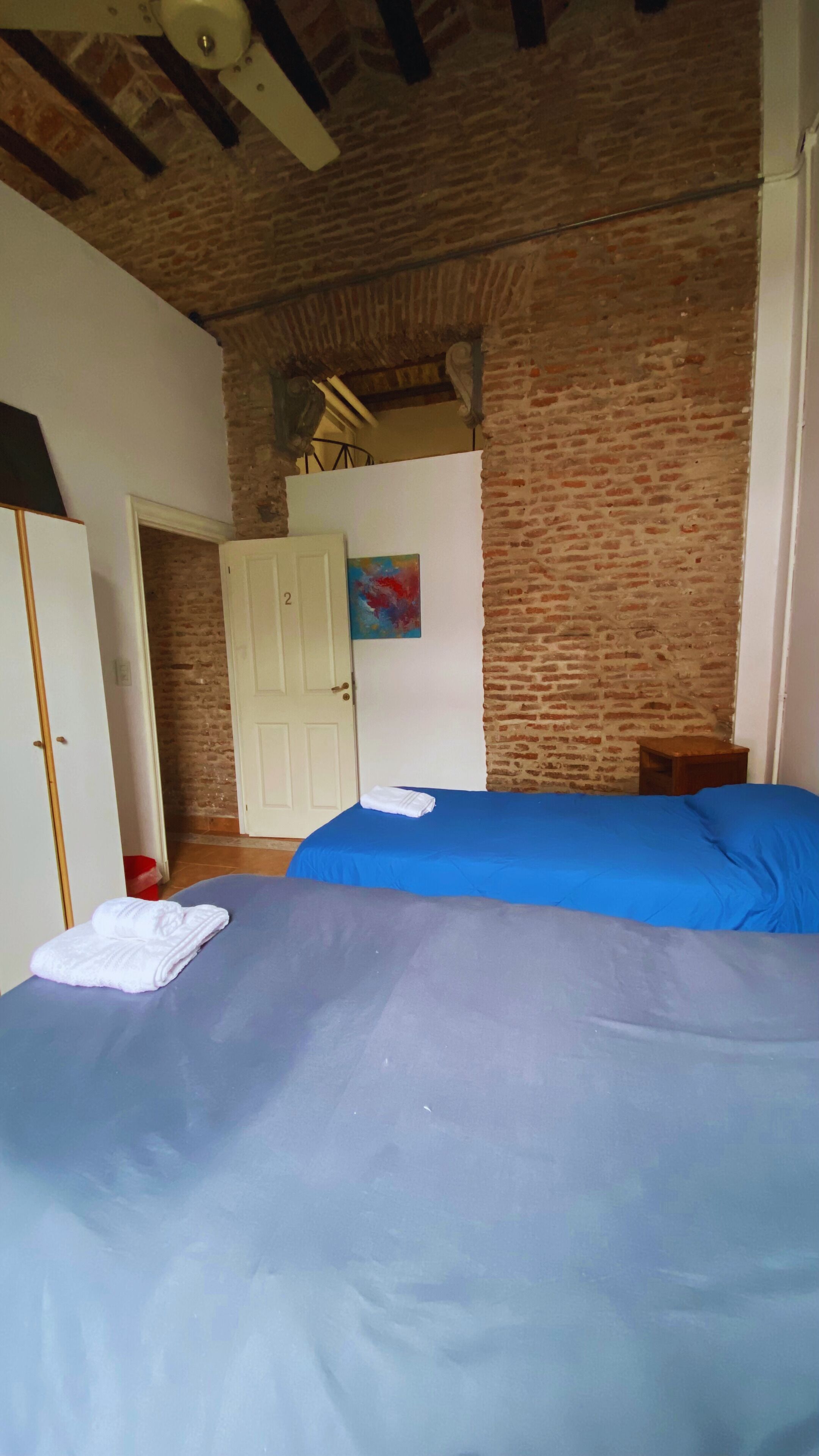 Un dormitorio con una cama, una puerta, un muro de ladrillo y un cuadro.