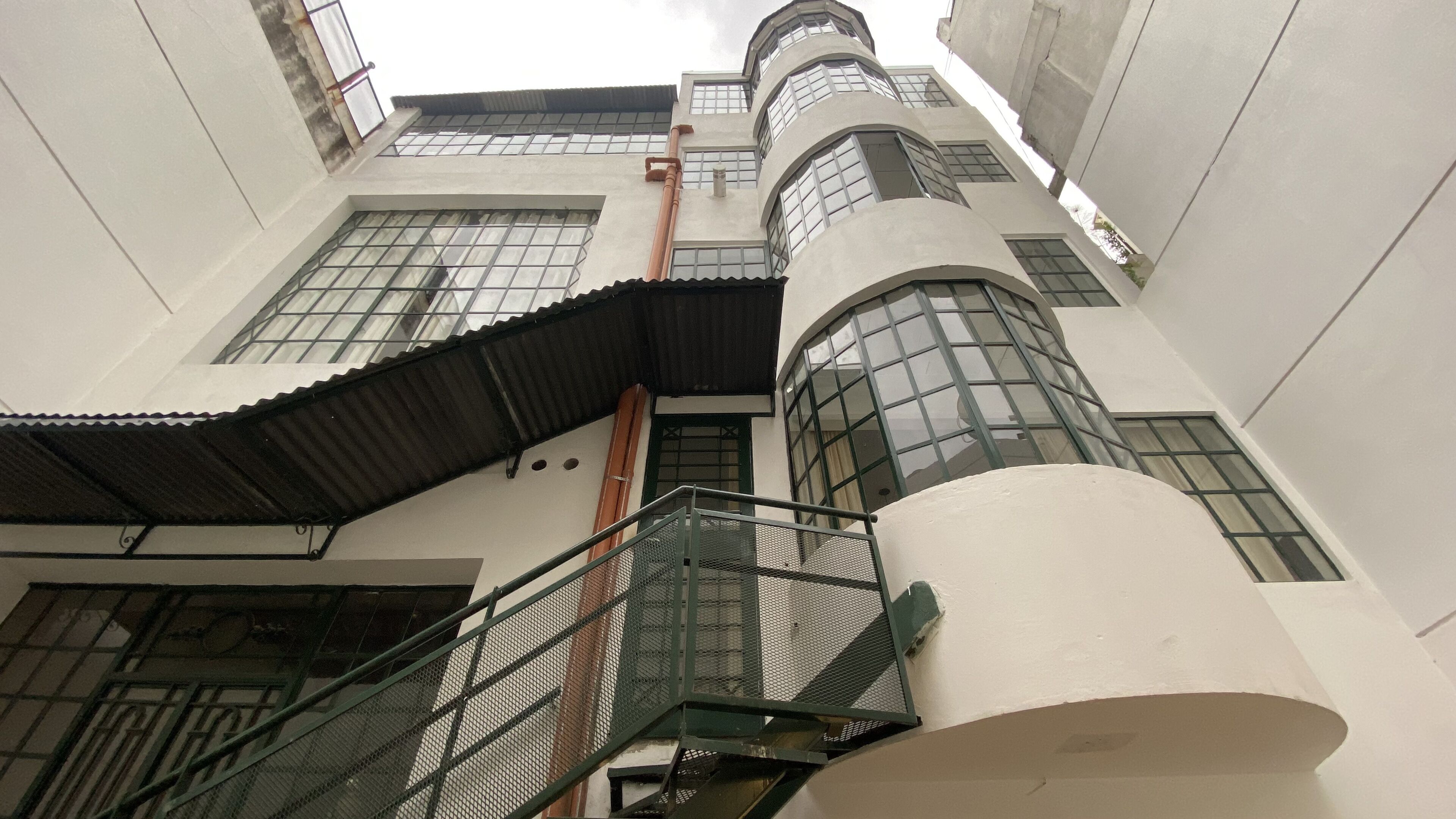 Un edificio de varios pisos con una escalera central, ventanas amplias y barandilla de metal.
