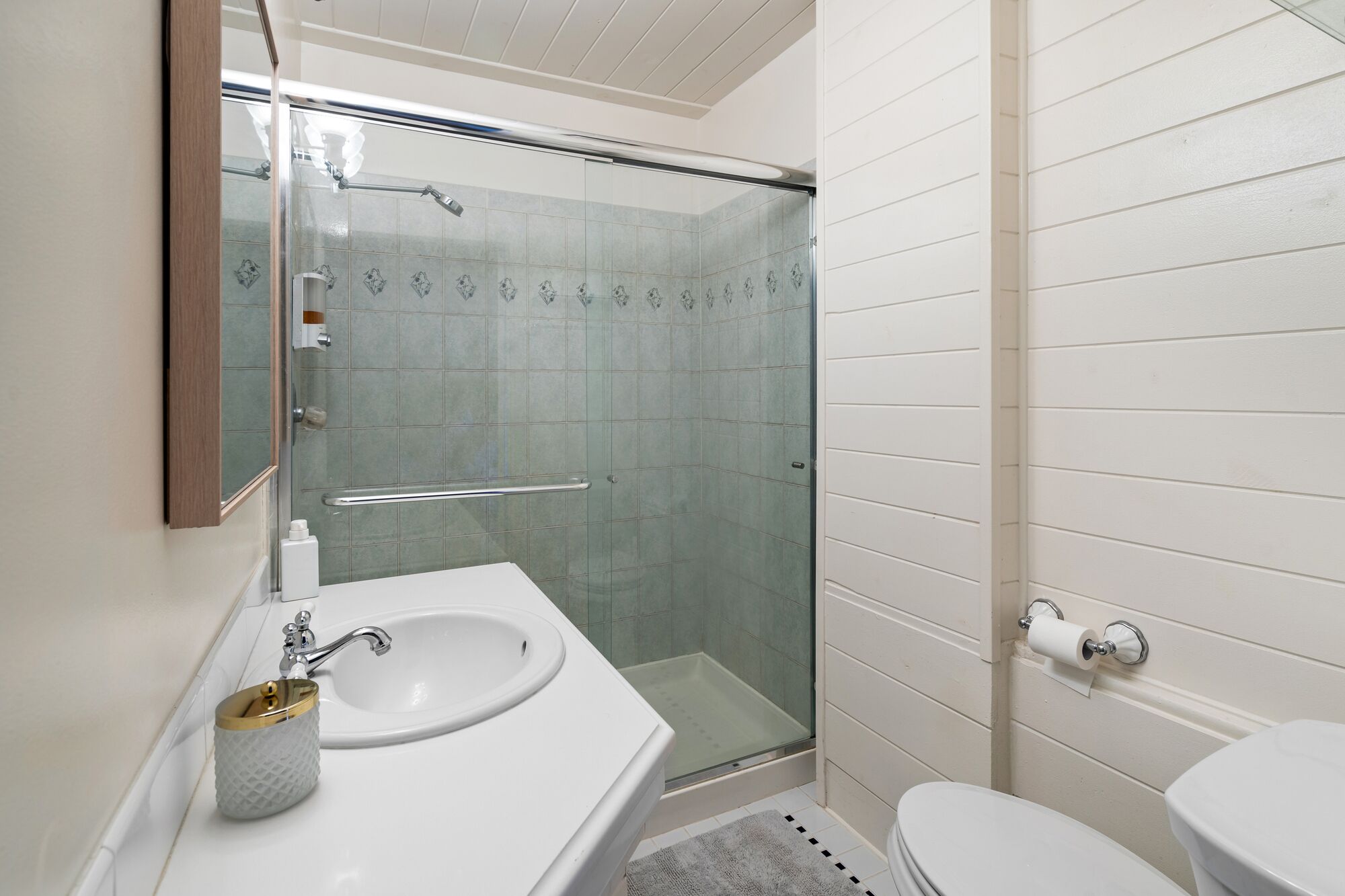 Een badkamer met een douchecabine van glas, een witte wastafel met zeepdispenser en een toilet.