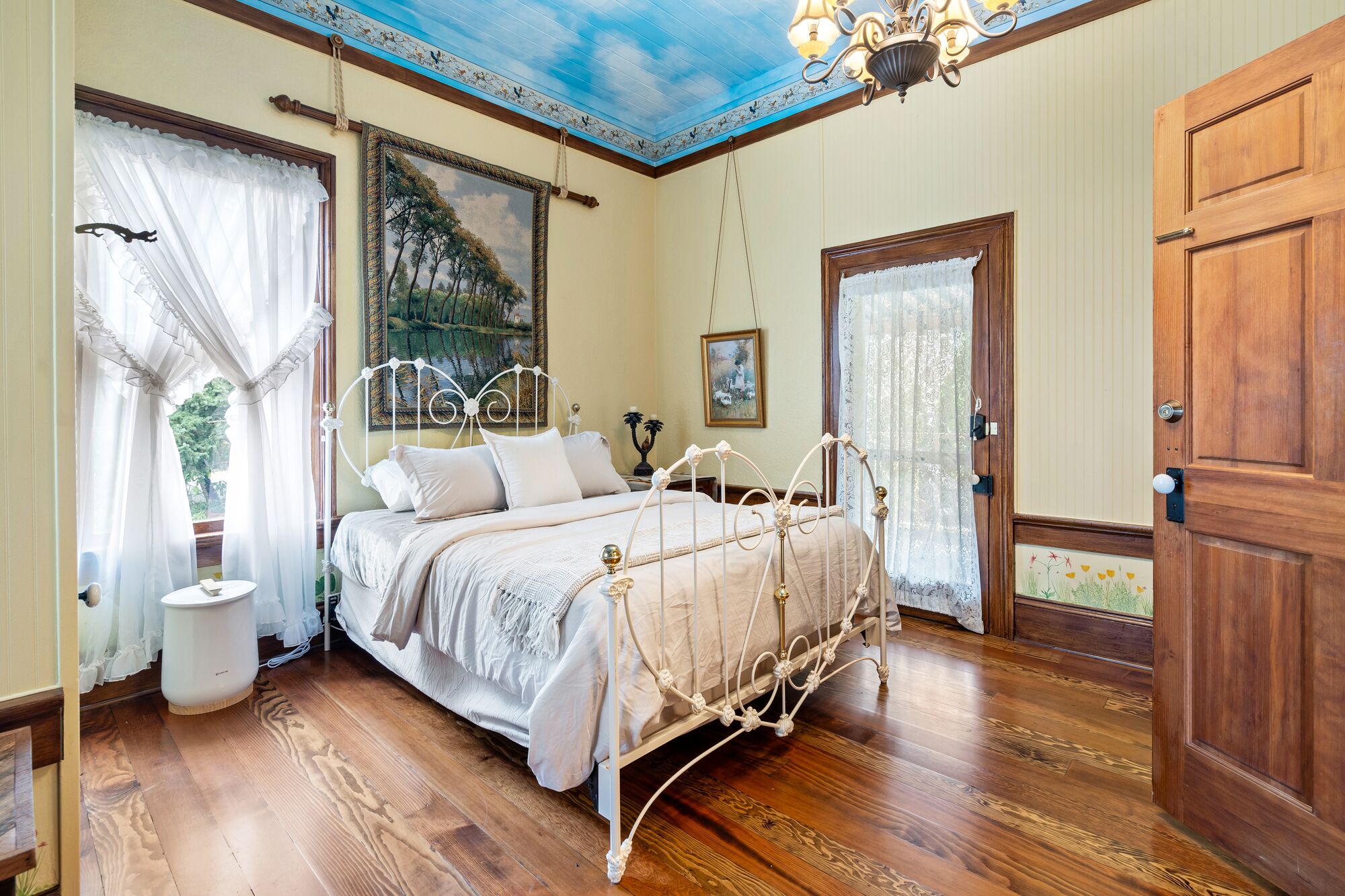 A bedroom with a wooden bed, a round bedside table, a chandelier, and a door with a floral design.
