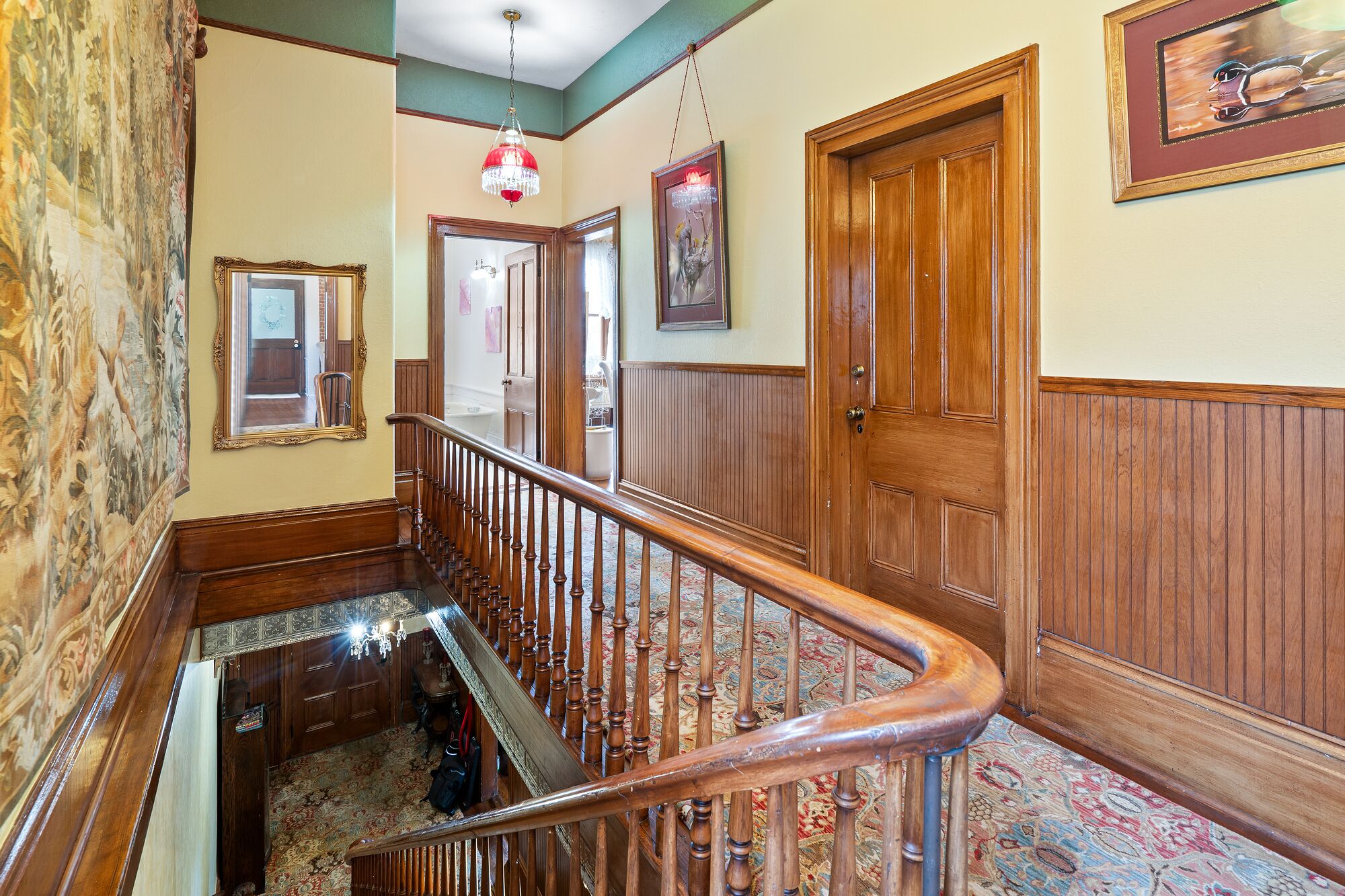 Un'imponente sala con una scala in legno, un lampadario e un grande quadro appeso al muro.