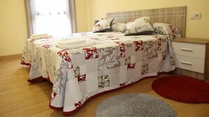 A neatly made bed with floral bedding, a bedside table, and a red rug on a wooden floor. - Alojamiento Caldas de Reis - Pensión (Caldas de Reis)