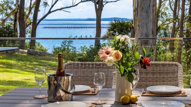 Ett vackert dukat bord med utsikt över havet, en flaska champagne och en vas med blommor.