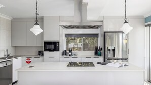 A modern kitchen with white cabinetry, a large island, a Bosch microwave, a coffee maker, and a stainless steel refrigerator. - Spacious Woodlands Water Front Soldiers Point- Ground Floor Apartment (Soldiers Point)