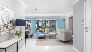 A modern living room with a dining area, a large window, and a view of the outdoors. - Spacious Woodlands Water Front Soldiers Point- Ground Floor Apartment (Soldiers Point)