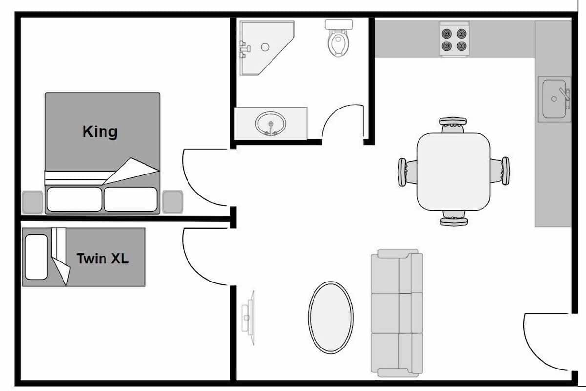 Une chambre d’hôtel comprenant un lit «king size», un lit simple «XL», une salle de bain avec des toilettes et un lavabo, une cuisine équipée d’une cuisinière et d’un évier, ainsi qu’un coin repas avec une table et des chaises.