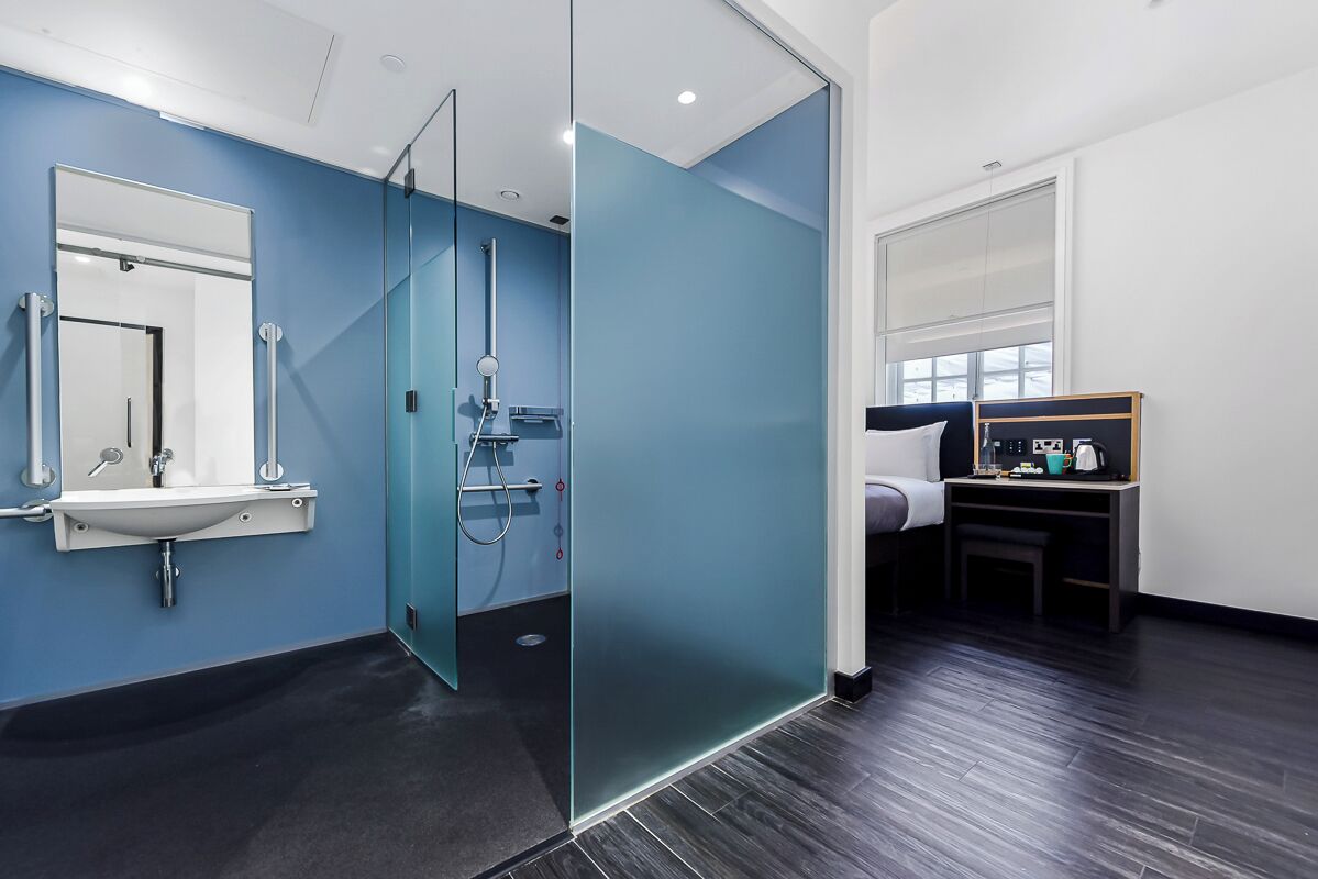 A modern bathroom with a glass shower enclosure, a sink with a mirror, and a bed with a nightstand.