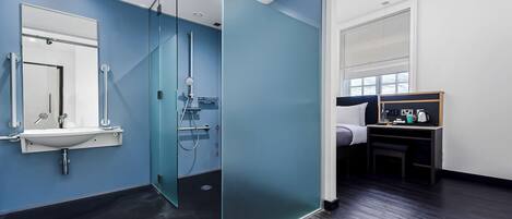 A modern bathroom with a glass shower enclosure, a sink with a mirror, and a bed with a nightstand.