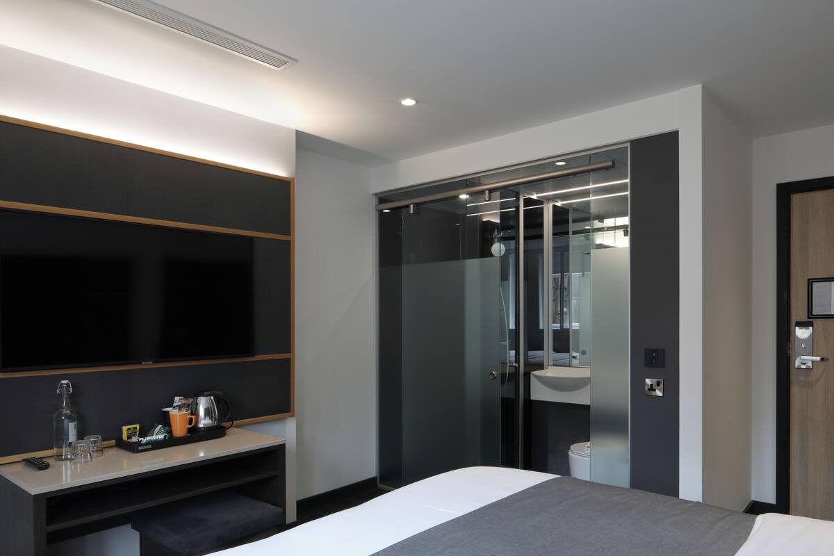Een moderne hotelkamer met een groot bed, een bureau met een flatscreen televisie, een douchecabine van glas en een houten deur.