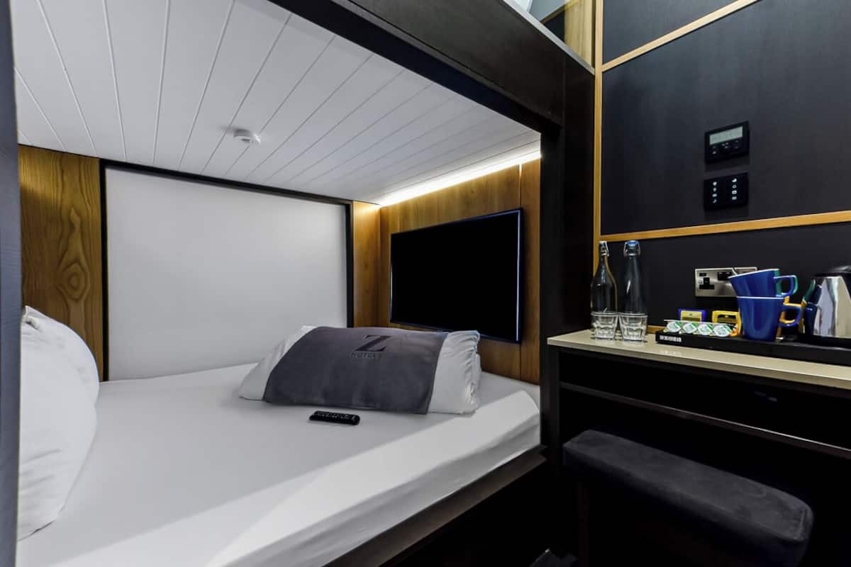 Een compacte hotelkamer met een eenpersoonsbed, een klein bureau en een televisie.