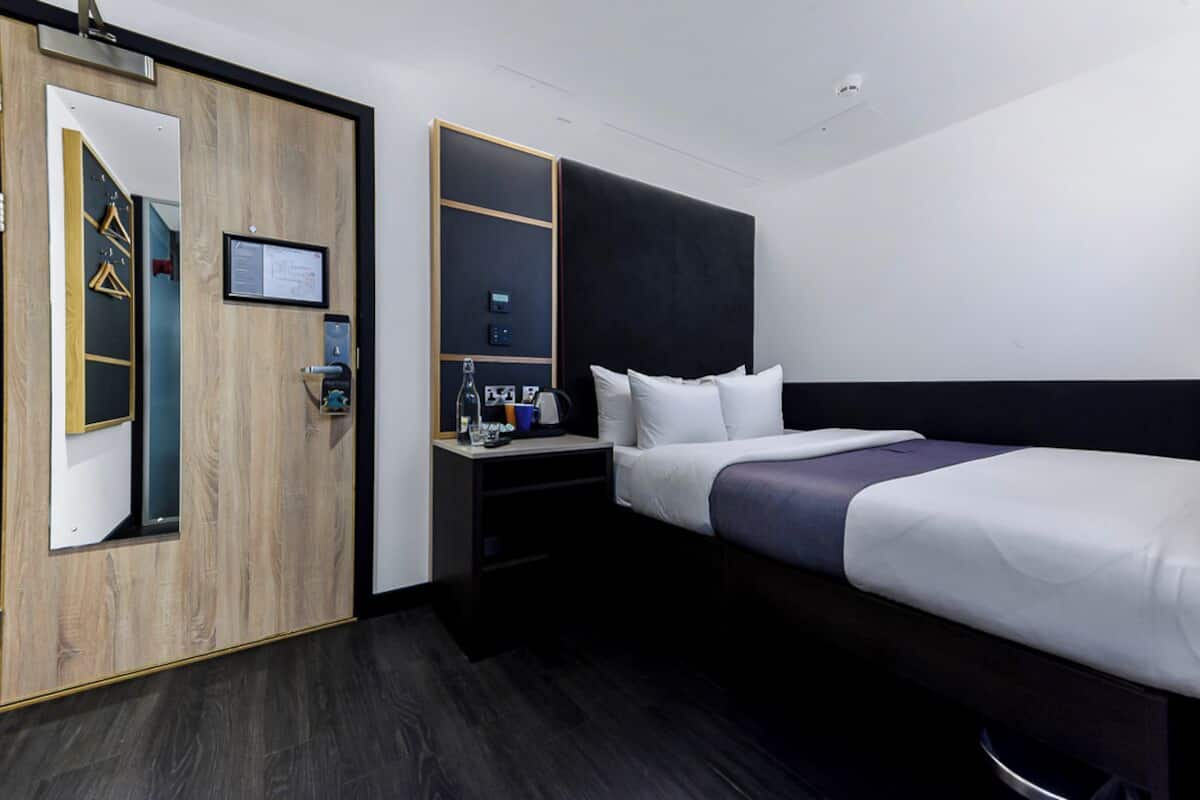 Een hotelkamer met een groot bed, een nachtkastje met een lamp, een garderobe en een spiegel.