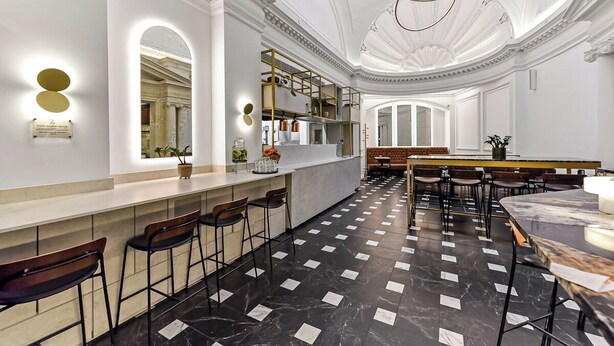 Een moderne bar met marmeren vloer, barstoelen en een zithoek met tafels en stoelen.