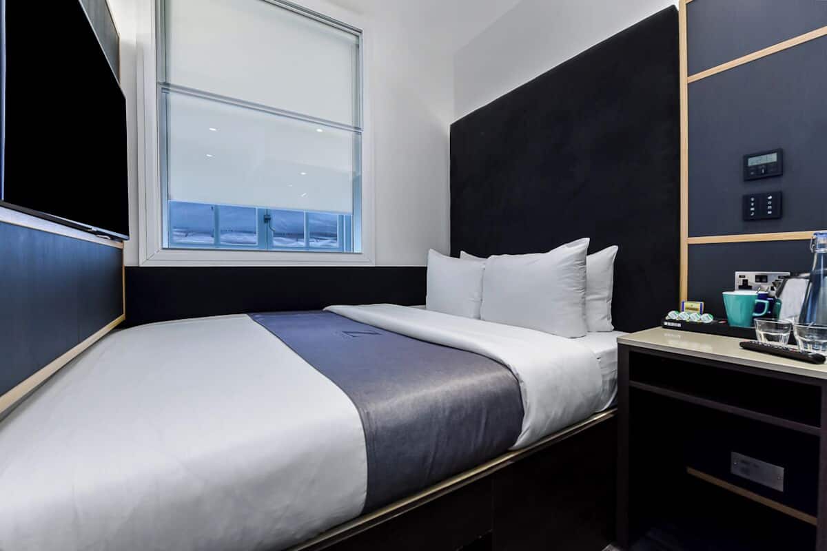 Een moderne hotelkamer met een groot bed, een raam met uitzicht, een bedieningspaneel en een bureau met een koffieapparaat.