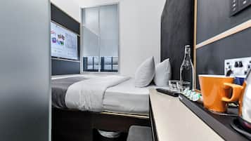 Ein gemütliches Schlafzimmer mit einem Bett, einem kleinen Tisch mit Flasche, Gläsern und Tasse, sowie einem Fernseher, der eine Programmvorschau zeigt.