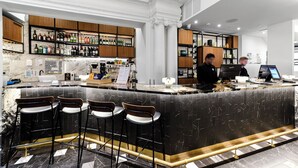 Een bar met een marmeren aanrecht, barkrukken en flessenkasten.