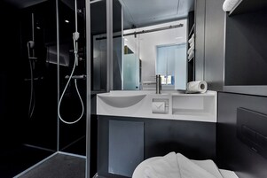 A modern bathroom with a glass shower enclosure, a white sink with a mirror above it, and a towel rack.