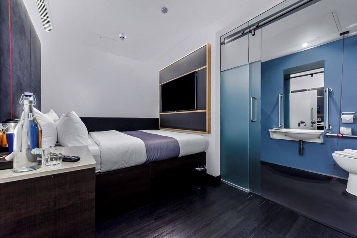 Een moderne hotelkamer met een bed, nachtkastje en een badkamer met wastafel en spiegel.