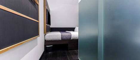 A narrow, modern room with a bed, a small bench, and a wall-mounted rack.